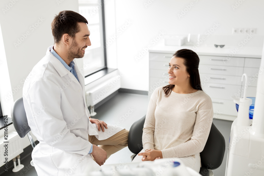 Fototapeta premium medicine, dentistry and healthcare concept - male dentist talking to female patient and discussing teeth treatment at dental clinic office