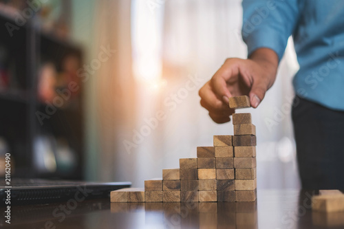 Businessman planing and strategy putting wooden blocks risk or success project stack of danger tower hands playing challenge game building construction protect at office. photo