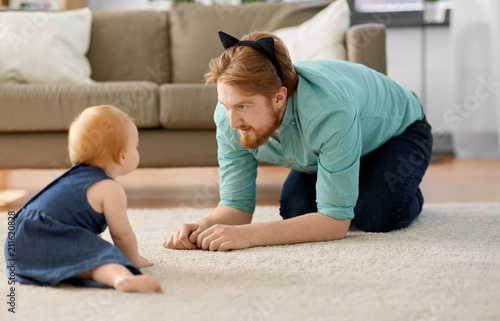 family, fatherhood and people concept - happy red haired father wearing cat ears headband playing with little baby daughter at home