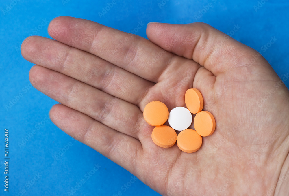 colorful pills on a female hand on a blue background, top view colorful pills on a female hand on a blue background, top view