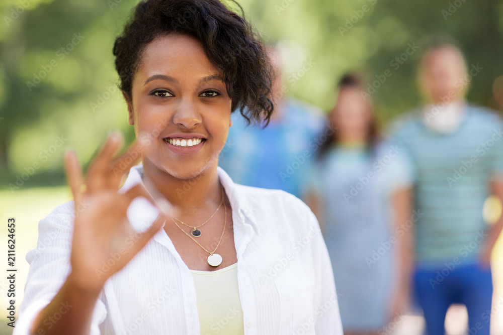 people, friendship and international concept - happy smiling woman showing ok hand sign and group of happy friends outdoors people, friendship and international concept - happy smiling woman showing ok hand sign and group of happy friends outdoors