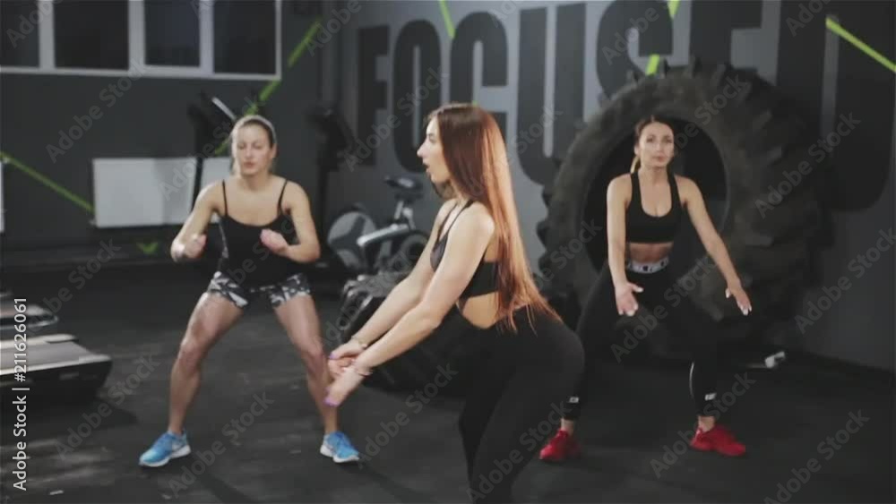 Group of young athletic women working out and squatting in team while training together in modern gym. Group of young athletic women working out and squatting in team while training together in modern gym.