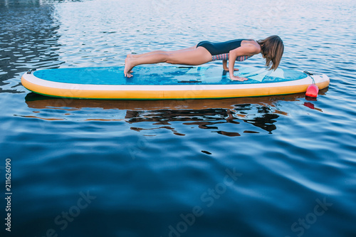 Young woman doing plank exercise on paddleboard