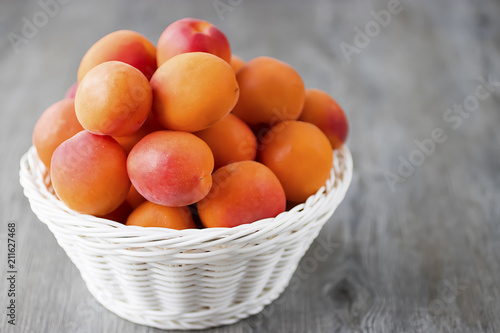 Ripe bright apricots in white basket on gray wooden background.