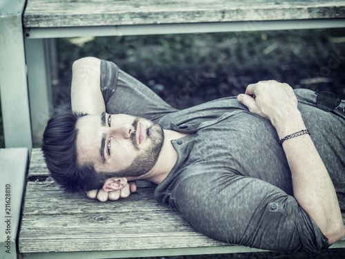 Attractive young man in city park in a nice summer day, laying on wood bench