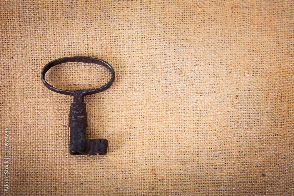 An ancient metal key on the background of sacking. An ancient metal key on the background of sacking.