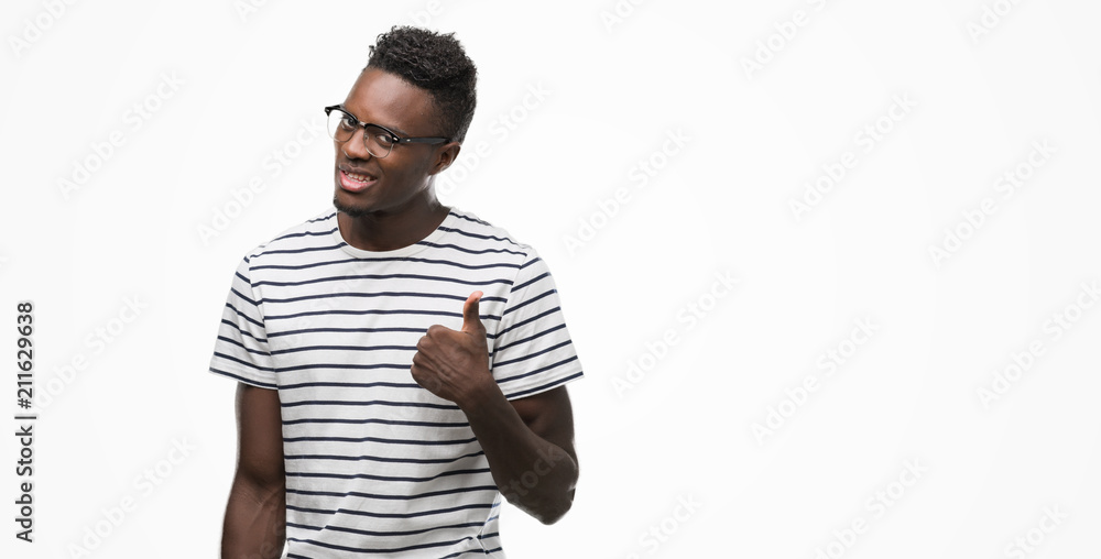 Young african american man wearing glasses and navy t-shirt doing happy thumbs up gesture with hand. Approving expression looking at the camera with showing success. Young african american man wearing glasses and navy t-shirt doing happy thumbs up gesture with hand. Approving expression looking at the camera with showing success.