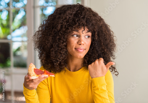 African american woman ready to eat pepperoni pizza slice pointing with hand and finger up with happy face smiling © Krakenimages.com