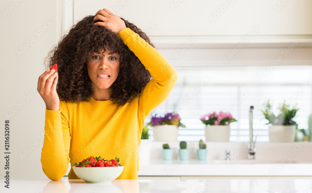 African american woman eating strawberries at home stressed with hand