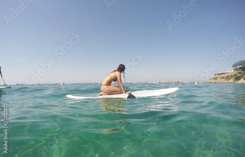 Chica con tabla de padel surf en playa de agua turquesa