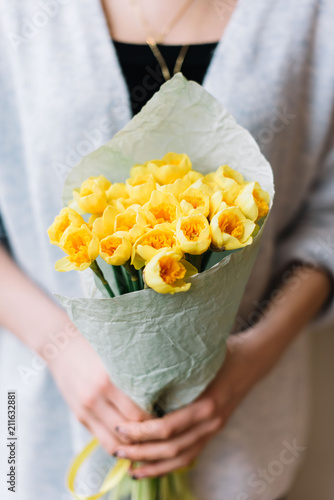Fototapeta Naklejka Na Ścianę i Meble -  Very nice young woman holding beautiful fresh blossoming bouquet yellow Narcissus on the grey background