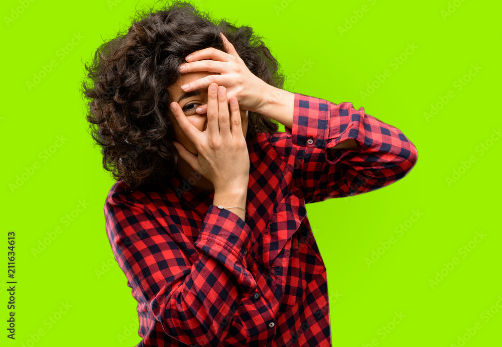 Beautiful arab woman smiling having shy look peeking through fingers, covering face with hands looking confusedly broadly Beautiful arab woman smiling having shy look peeking through fingers, covering face with hands looking confusedly broadly