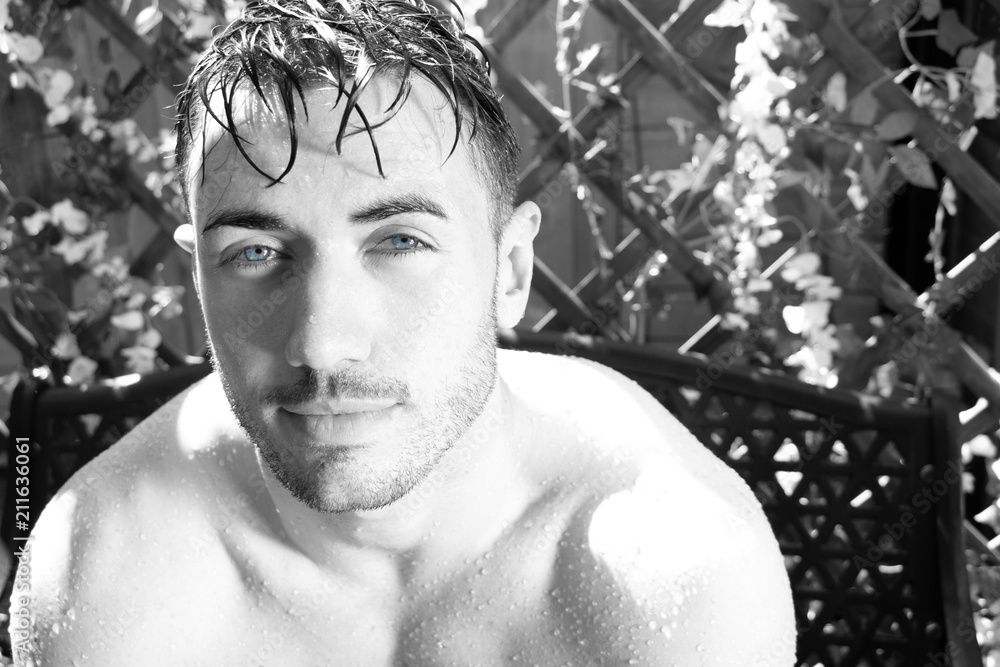 Handsome semi naked man with muscles and bare chest caught in shower of rain in garden with wet