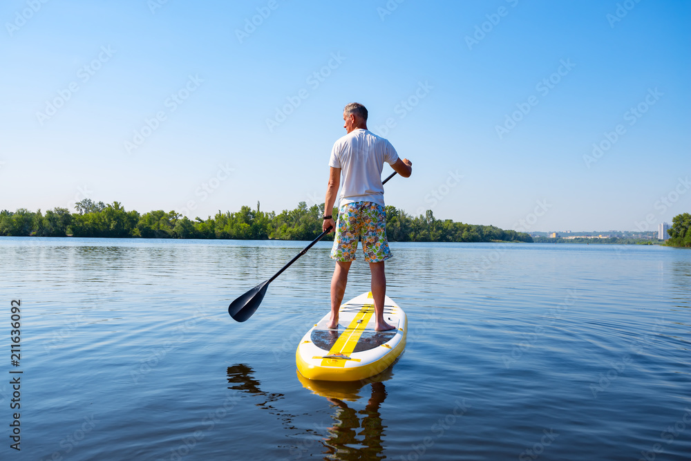 Adult man sails on a SUP board in large river