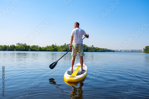 Obraz na płótnie Adult man sails on a SUP board in large river w salonie