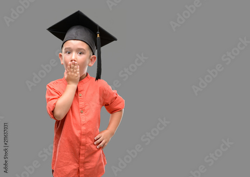 Dark haired little child wearing graduation cap cover mouth with hand shocked with shame for mistake, expression of fear, scared in silence, secret concept