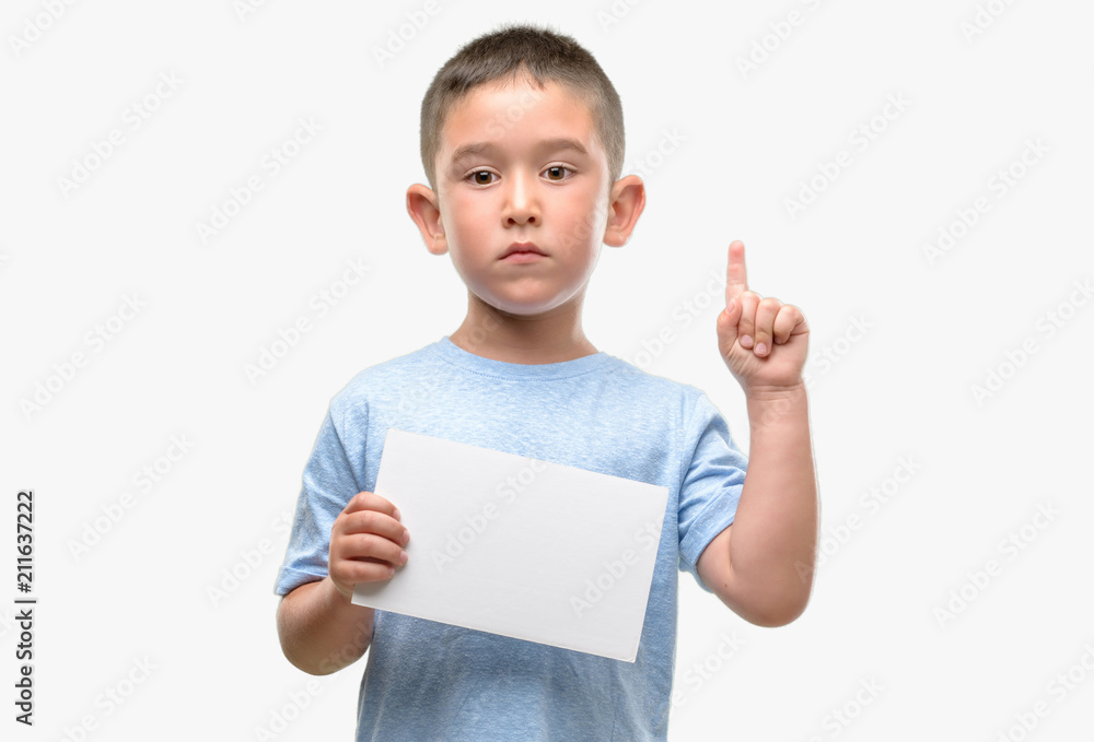 Dark haired little child holding a blank card surprised with an idea or question pointing finger with happy face, number one Dark haired little child holding a blank card surprised with an idea or question pointing finger with happy face, number one