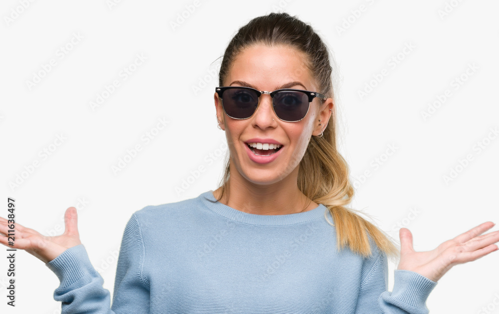 Beautiful young woman wearing sunglasses and ponytail very happy and excited, winner expression celebrating victory screaming with big smile and raised hands Beautiful young woman wearing sunglasses and ponytail very happy and excited, winner expression celebrating victory screaming with big smile and raised hands
