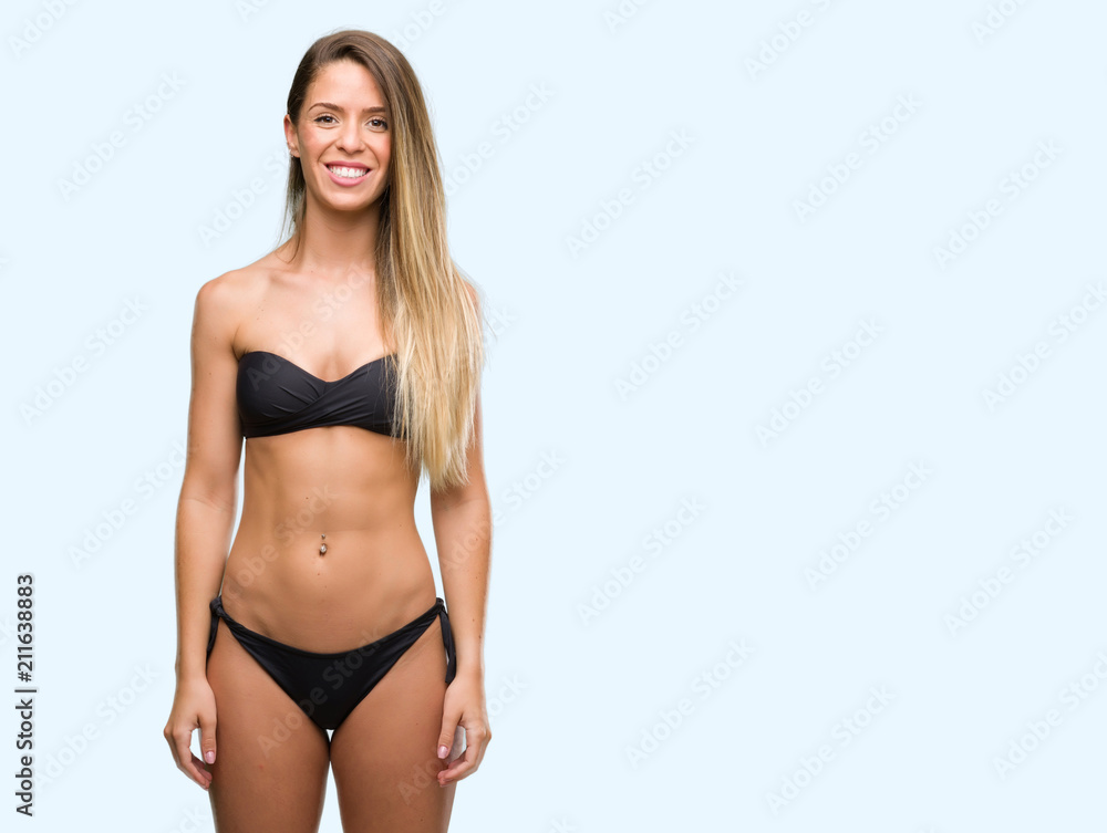 Naklejka premium Beautiful young woman wearing black bikini with a happy face standing and smiling with a confident smile showing teeth