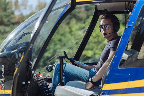 Skilled professional. Athletic young pilot sitting at a pilot booth of a helicopter and posing for the camera, being ready to start a flight
