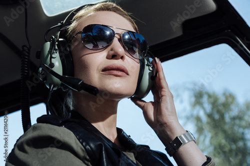 Gorgeous professional. The close up of a pretty young female helicopter pilot sitting listening to air traffic controller in her headphones and being ready to start a flight