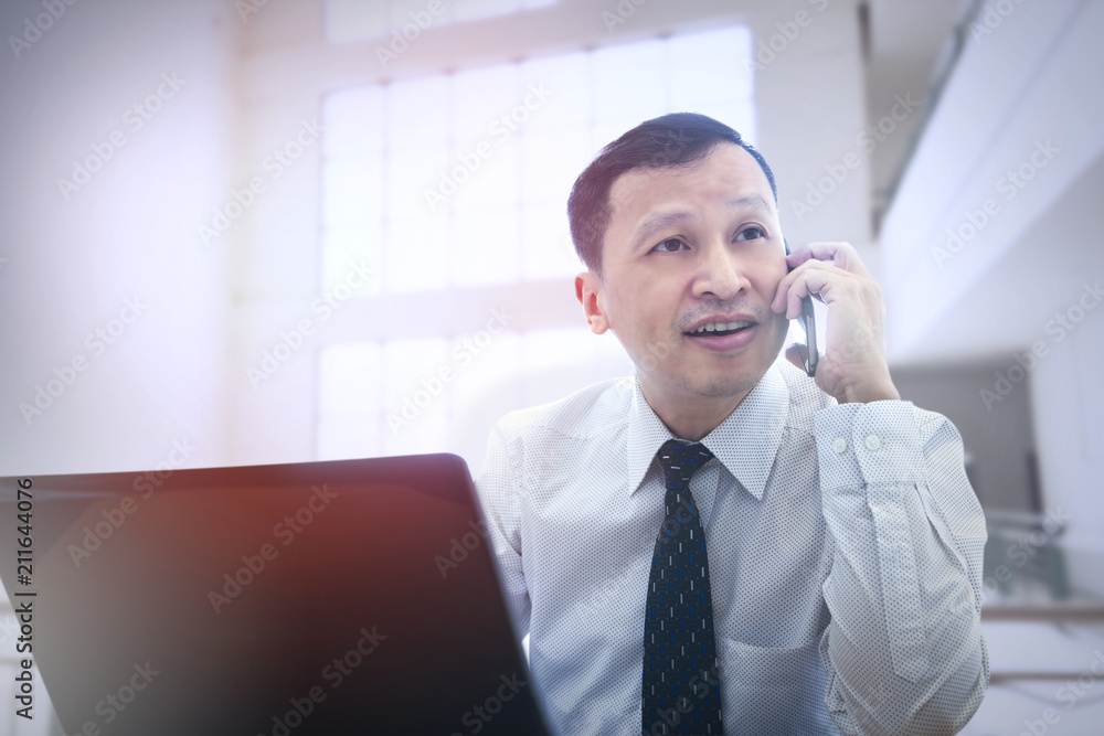 Asian businessman using mobie phone and notebook computer indoor with upper copy space. Asian businessman using mobie phone and notebook computer indoor with upper copy space.