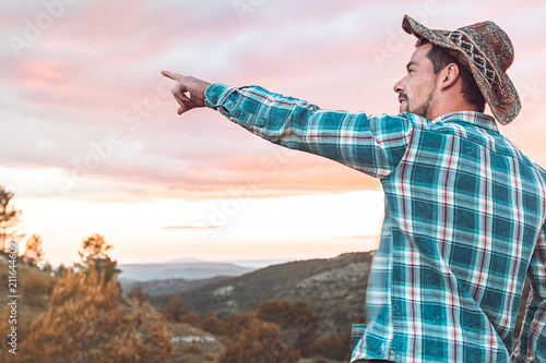 Guy pointing to the horizon in the mountain in casual dress