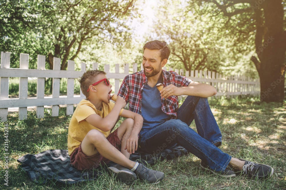 Another cool picture of adult and child sitting together and looking at each other. They are eating ice cream. Small boy wears glasses. Another cool picture of adult and child sitting together and looking at each other. They are eating ice cream. Small boy wears glasses.