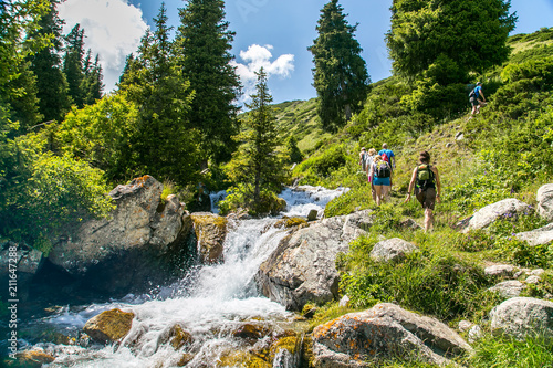 Tourist group in the mountains near the river. Trees,  rocks around the mountain river.  Hiking in Kyrgyzstan.