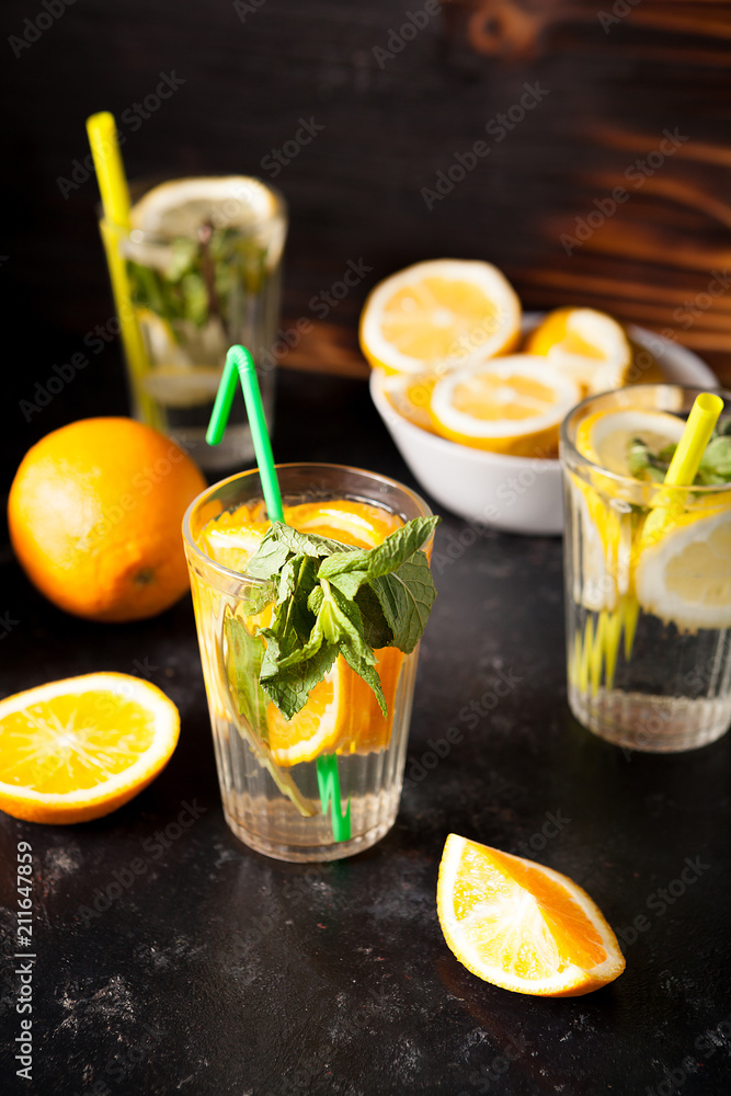 Healthy and delicous detox water made of lemons and oranges next to cutted fruits on dark vintage wooden background Healthy and delicous detox water made of lemons and oranges next to cutted fruits on dark vintage wooden background