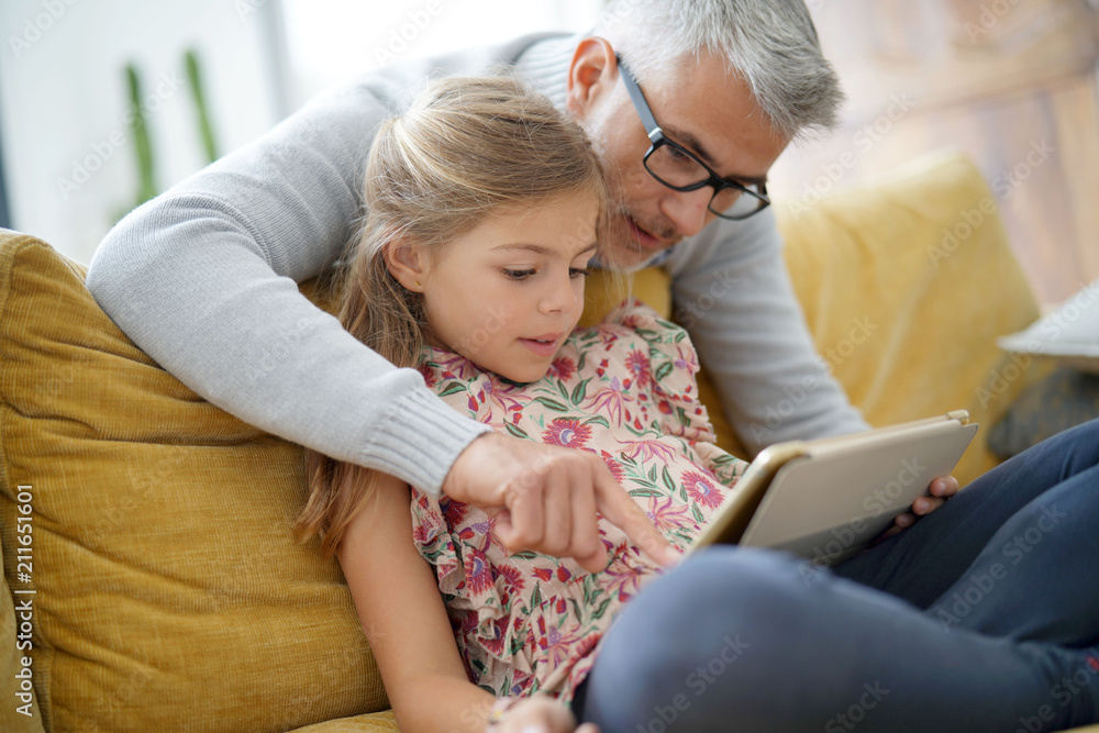 Father and daughter connected with tablet, sitting on couch
