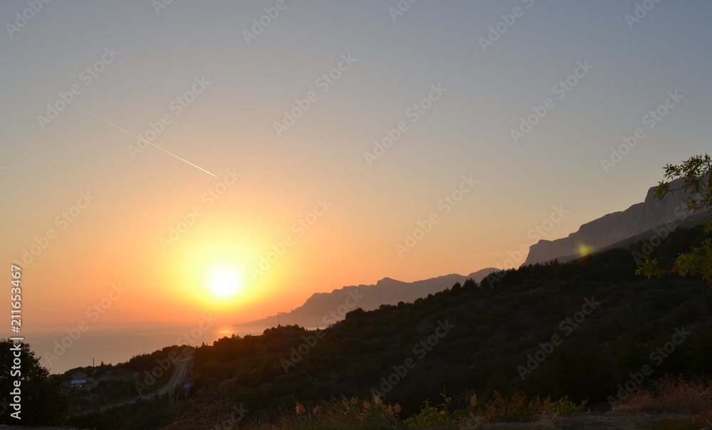 Sunset, setting sun over the sea and mountains, purple colors.