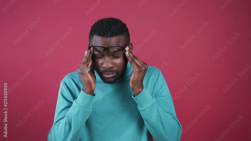 Young tired African man in casual clothes touching head, taking off glasses. Portrait of attractive guy in mint sweater on background of pink wall. Headache. Young tired African man in casual clothes touching head, taking off glasses. Portrait of attractive guy in mint sweater on background of pink wall. Headache.