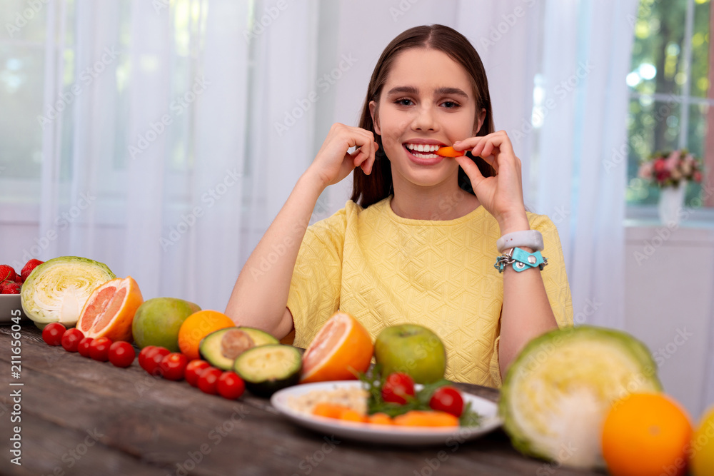 Juicy vegetable. Low angle of glad teen girl eating carrot and looking at camera Juicy vegetable. Low angle of glad teen girl eating carrot and looking at camera