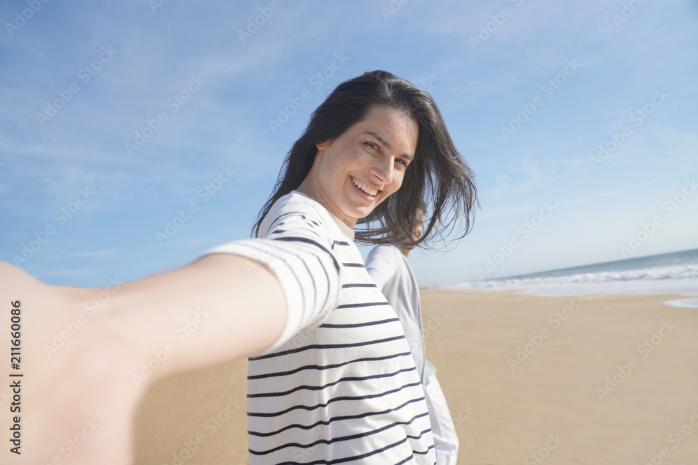 Cheerful brunette woman wallking on the beach, leading camera towards her Cheerful brunette woman wallking on the beach, leading camera towards her