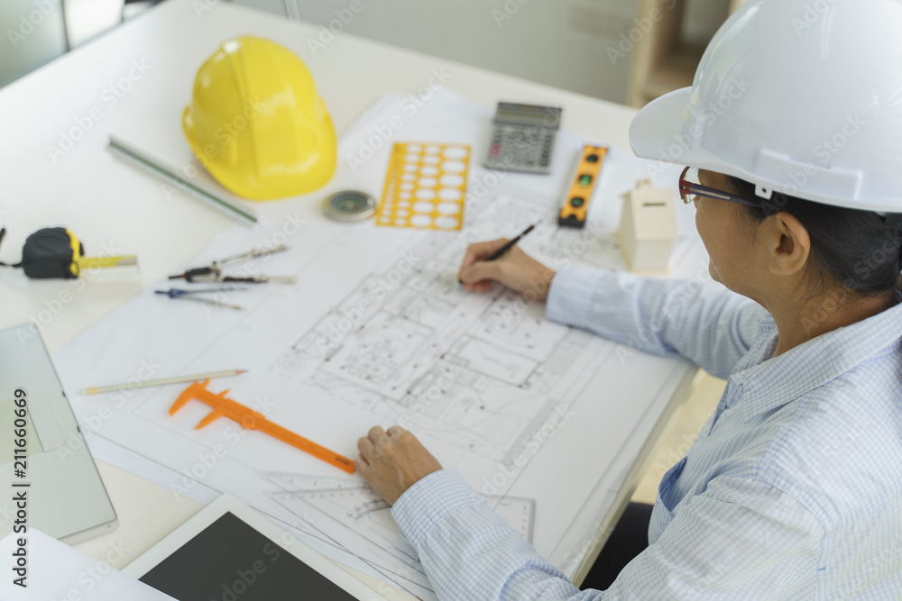 Top view, Woman Architect or engineer hands working on blueprint plans with a pencil ,laptop a ruler, calculator, and engineering tools. Architect or engineer working on blueprint in office. Top view, Woman Architect or engineer hands working on blueprint plans with a pencil ,laptop a ruler, calculator, and engineering tools. Architect or engineer working on blueprint in office.