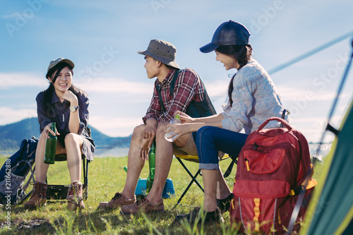 Asian group friends travel camping together in forest with backpack and tent picnic drinks beer,water at nature outdoor young teenager talking relax,rest near mountain view.