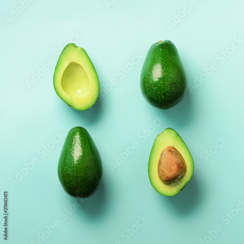 Organic avocado with seed, avocado halves and whole fruits on blue background. Top view. Pop art design, creative summer food concept. Green avocadoes pattern in minimal flat lay style.