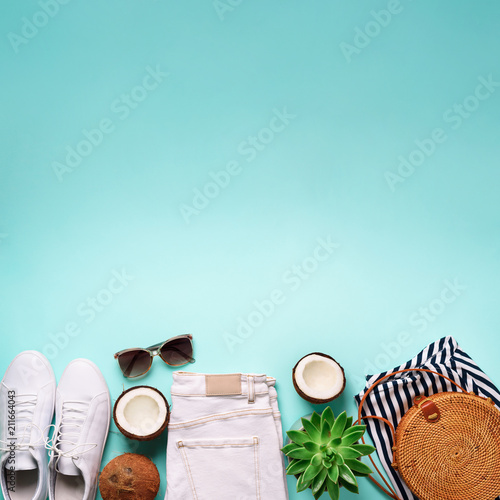 Woman summer travel clothes travel on blue background. Jeans, sneakers, bamboo bag, sunglasses, coconut and succulent. Top view, flat lay. Fashion, capsule wardrobe concept. Creative flat lay. © jchizhe