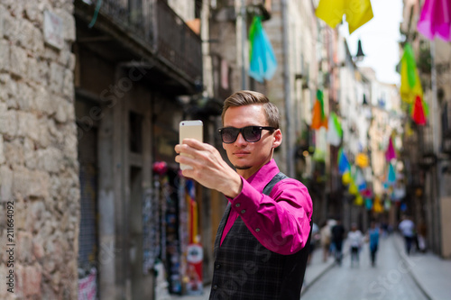 A young guy, a tourist does selfie on a mobile phone in the street Girona, decorated with colorful shawls