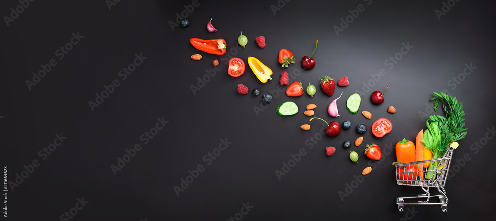Fototapeta Wózek sklepowy wypełniony świeżymi organicznymi warzywami, owocami i jagodami na czarnej tablicy. Widok z góry. Wegetariańskie, wegańskie, detoksykacyjne i czyste jedzenie