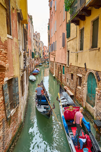 Venetian gondolier punting gondola through canal in Venice, Italy