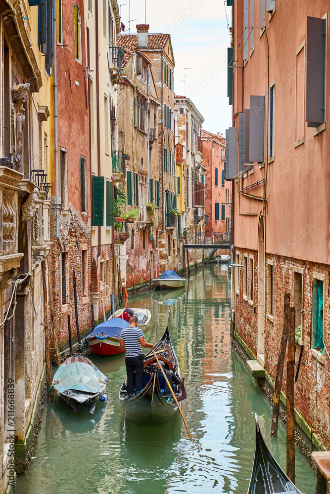 Venetian gondolier punting gondola through canal in Venice, Italy
