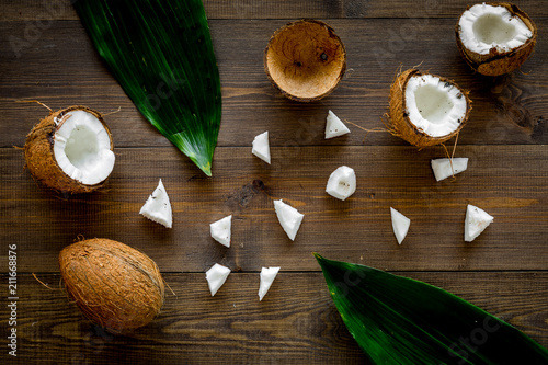 Coconut background. Whole and cut coconuts, pulp and palm leaves on dark wooden background top view