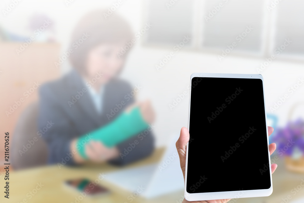 Hand holding tablet on blurred blackground injured woman with broken hand sitting and holding green cast working with laptop in office Hand holding tablet on blurred blackground injured woman with broken hand sitting and holding green cast working with laptop in office