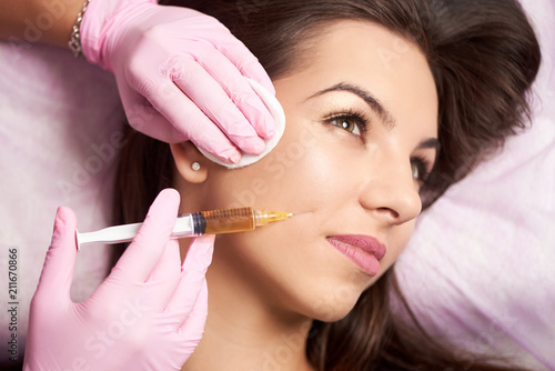 Close-up of beautiful woman getting injection in the cosmetology salon. Doctor in medical gloves with syringe injects cheeks drug.