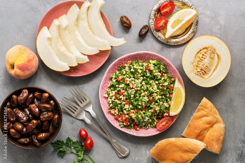 Middle Eastern or Arabic dish tabbouleh salad with pita bread on a gray background. Oriental sweets and fruits,melon, peaches , dates.Top view