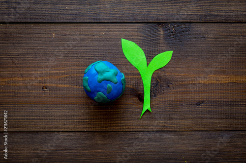 Planet, ecology. plastiline symbol of planet Earth globe and plant coutout on dark wooden background top view copy space photo