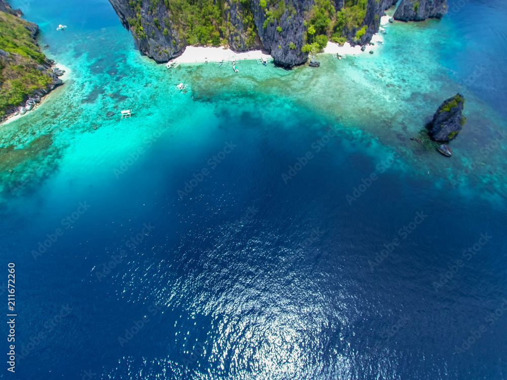 The azure blue sea. Top view of a tropical island with palm trees and blue clear water. Aerial view of a white sand beach and boats over a coral reef. The island of Palawan, Philippines.