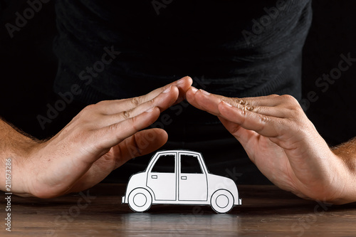 The concept of car insurance, a man covers a car with paper hands, close-up.